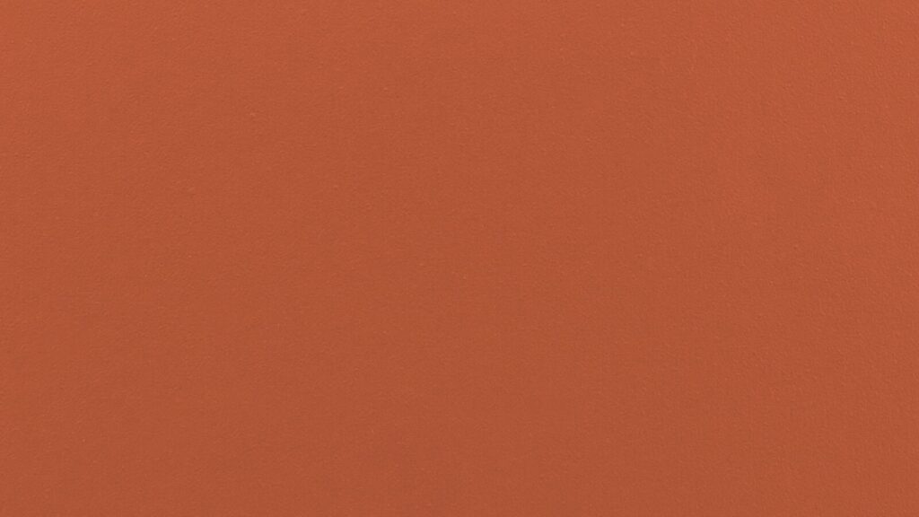 A smooth, solid orange surface. The texture appears even and consistent, with no visible patterns or designs. The shade of orange is bright and vibrant.